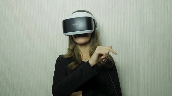 Mulher usando o dedo para tocar na visualização de painel imaginário no dispositivo VR contra a parede branca. Uso da menina do dispositivo do vr — Fotografia de Stock