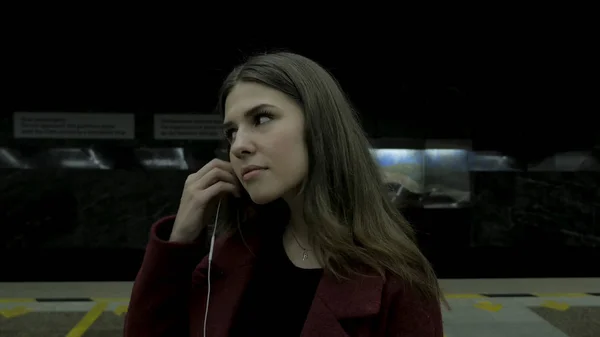 Fiatal lány hallgat zenét a fejhallgatót a metró alagútban. Fiatal női diák, hallgató-hoz zene nagy fejhallgató a metró alagútban. Fiatal nő a smartphone-on zenét hallgat a — Stock Fotó