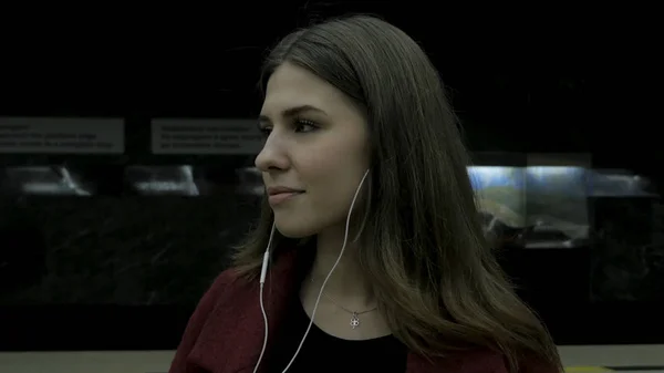 Young girl listens to music in headphones in the subway tunnel. Young female student listening to music in big headphones in the subway tunnel. Young woman listening to music on her smartphone at the