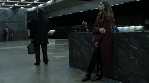 Красивая девушка с шапочкой слушает музыку на станции метро. Женщина, пользующаяся телефоном в метро, слушает музыку в наушниках. Тёмный портрет молодой женщины в метро. Поезд прибывает. — стоковое фото