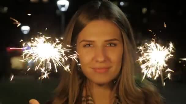 Havai fişekleri ile gece sokakta genç kız gülümsüyor. Genç kadın bir olay yeni yıl kutlama geliyor. Ağır çekimde tutan kız portresi parıldıyor — Stok video