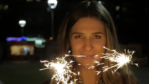 Sonriente adolescente en la calle por la noche con bengalas. Mujer joven celebrando un evento el Año Nuevo se acerca. Retrato de niña sosteniendo destellos en cámara lenta — Vídeo de stock