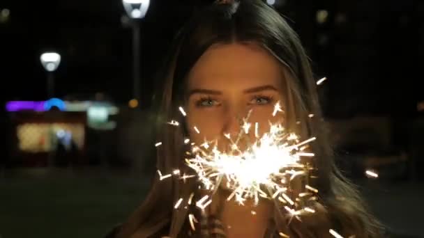 Menina sorrindo jovem segurando sparkler em sua mão. Retrato de menina segurando faíscas em câmera lenta — Vídeo de Stock