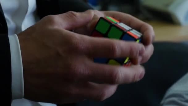 Podnikatel v obleku drží Rubiks cube. Podnikatel se snaží sestavit Rubiks cube closeup — Stock video
