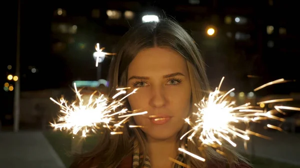 Schöne lächelnde junge Frau mit einer Wunderkerze in der Hand. Nachtszene. junges lächelndes Mädchen mit Wunderkerze in der Hand. Urlaubskonzept — Stockfoto