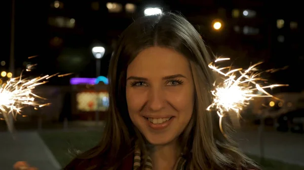 Bella giovane donna sorridente in possesso di una scintilla. Scena notturna. Giovane ragazza sorridente che tiene scintillante in mano. Concetto vacanza — Foto Stock