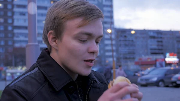 Young man eating biting a tasty fast food hamburger at street burger. Young man eating a Burger on the street — Stock Photo, Image