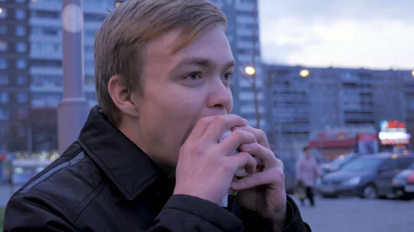 Junger Mann beißt in einen leckeren Fast-Food-Hamburger an einem Straßenburger. Junger Mann isst einen Burger auf der Straße — Stockfoto