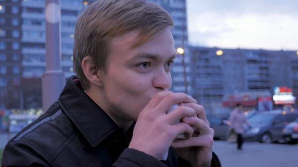 Nuori mies syö maukasta pikaruokahampurilaista katupurilaisella. Nuori mies syö hampurilaista kadulla. — kuvapankkivalokuva