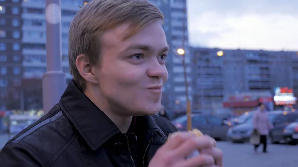 Jeune homme mangeant un hamburger de restauration rapide savoureux au hamburger de rue. Jeune homme mangeant un hamburger dans la rue — Photo