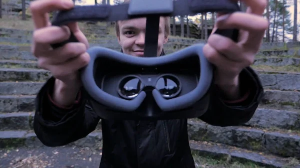 Ein junger Mann gibt im Park ein Virtual-Reality-Headset ab. junger Mann gibt Virtual-Reality-Headset im Freien — Stockfoto