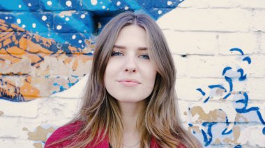 Mutlu genç kadın ayakta açık tuğla duvar, kameraya bakıyor. Duvarın yanında sokakta kameraya arayan genç çekici kadın