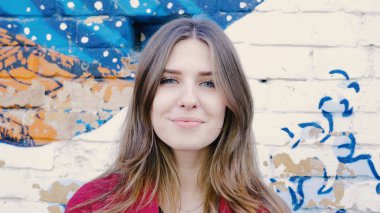 Mutlu genç kadın ayakta açık tuğla duvar, kameraya bakıyor. Duvarın yanında sokakta kameraya arayan genç çekici kadın