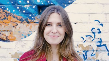 Mutlu genç kadın ayakta açık tuğla duvar, kameraya bakıyor. Duvarın yanında sokakta kameraya arayan genç çekici kadın