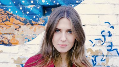 Mutlu genç kadın ayakta açık tuğla duvar, kameraya bakıyor. Duvarın yanında sokakta kameraya arayan genç çekici kadın