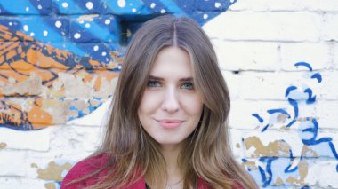 Mutlu genç kadın ayakta açık tuğla duvar, kameraya bakıyor. Duvarın yanında sokakta kameraya arayan genç çekici kadın