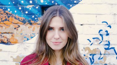 Mutlu genç kadın ayakta açık tuğla duvar, kameraya bakıyor. Duvarın yanında sokakta kameraya arayan genç çekici kadın