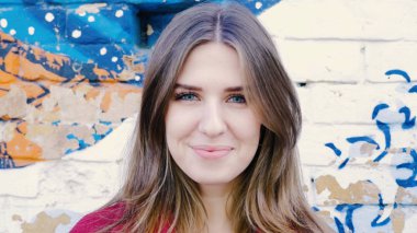 Mutlu genç kadın ayakta açık tuğla duvar, kameraya bakıyor. Duvarın yanında sokakta kameraya arayan genç çekici kadın