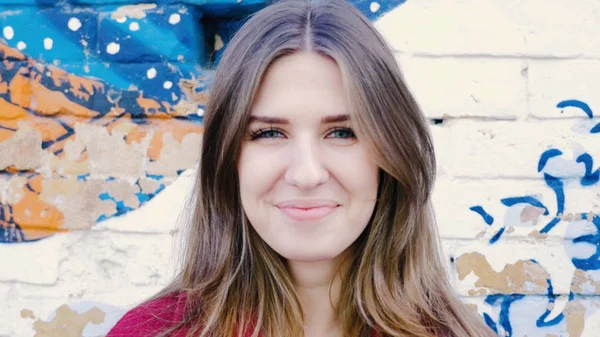 Mutlu genç kadın ayakta açık tuğla duvar, kameraya bakıyor. Duvarın yanında sokakta kameraya arayan genç çekici kadın