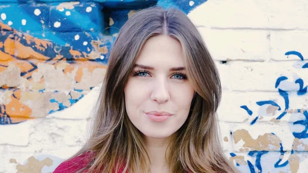 Mutlu genç kadın ayakta açık tuğla duvar, kameraya bakıyor. Duvarın yanında sokakta kameraya arayan genç çekici kadın