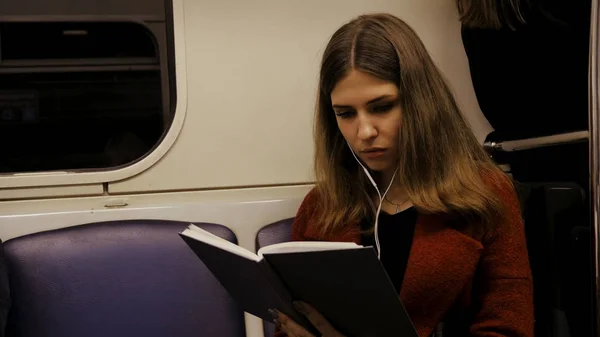 Gyönyörű fiatal nő ül a metró olvasó egy könyv - ingázó, a diák, a tudás fogalma. Fiatal nő a metróban a könyvet olvas — Stock Fotó