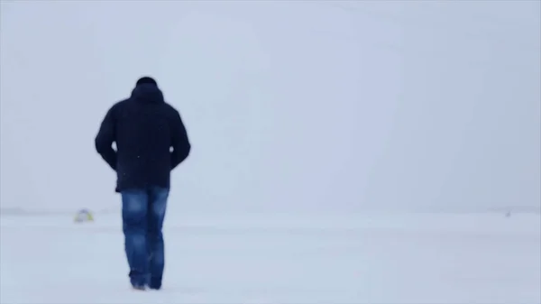 Man walking in snow. Man walking on snow, footprints in snow, behind. Man walks in the winter in the field