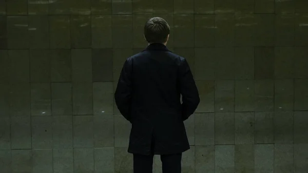 Yksinäinen nuori mies takaa metroasemalta. Nuori mies odottaa junaa metrossa, näkymä taakse — kuvapankkivalokuva