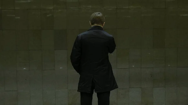 Yksinäinen nuori mies takaa metroasemalta. Nuori mies odottaa junaa metrossa, näkymä taakse — kuvapankkivalokuva