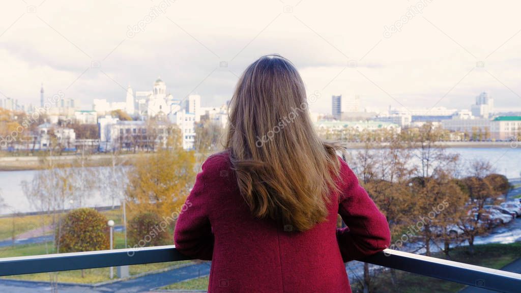 Rear view of woman standing on balcony and enjoying the view on the city. Back view of young woman standing on the balcony