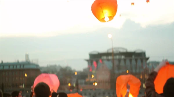 From beneath young woman being in city holding burning chinese lantern want to launch it to evening sky. Young woman launches a sky lantern — Stock Photo, Image