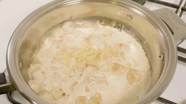 Draufsicht auf das Hinzufügen von Käse in die Pfanne mit dem Huhn. Hühnchen in der Pfanne braten. Großaufnahme von Hühnerfleisch, das auf einer heißen Pfanne auf einem Gasherd kocht — Stockfoto
