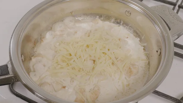 Draufsicht auf das Hinzufügen von Käse in die Pfanne mit dem Huhn. Hühnchen in der Pfanne braten. Großaufnahme von Hühnerfleisch, das auf einer heißen Pfanne auf einem Gasherd kocht — Stockfoto