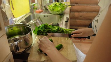 Kadın mutfakta salata hazırlanıyor. Çekici kız kesim salatalık salatası mutfağında evde yaparken. Genç kadın mutfakta bir salatalık keser