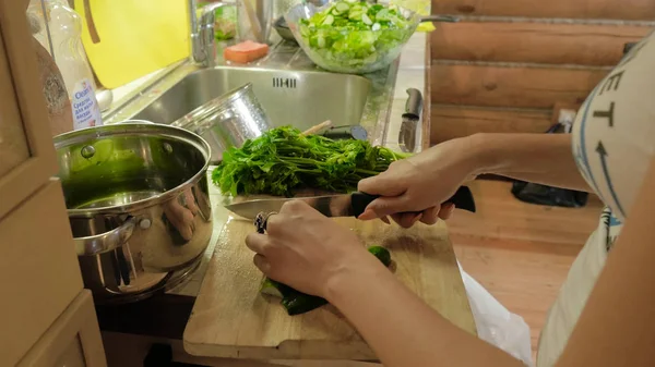 Kadın mutfakta salata hazırlanıyor. Çekici kız kesim salatalık salatası mutfağında evde yaparken. Genç kadın mutfakta bir salatalık keser