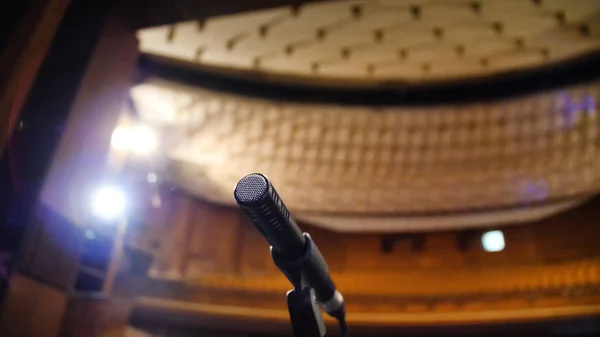 Micrófono en el escenario y sala vacía durante el ensayo. Micrófono en el escenario con luces de escenario en el fondo. Micrófono en el escenario en la sala vacía —  Fotos de Stock