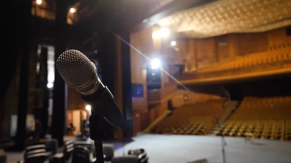 Micrófono en el escenario y sala vacía durante el ensayo. Micrófono en el escenario con luces de escenario en el fondo. Micrófono en el escenario en la sala vacía —  Fotos de Stock