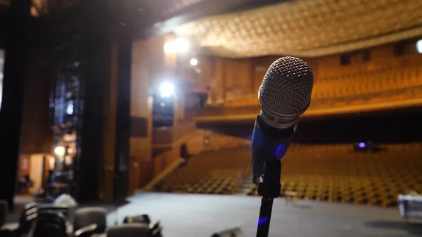 Mikrofon di atas panggung dan aula kosong selama latihan. Mikrofon di atas panggung dengan lampu panggung di latar belakang. Mikrofon di atas panggung di aula kosong — Stok Foto