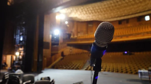 Micrófono en el escenario y sala vacía durante el ensayo. Micrófono en el escenario con luces de escenario en el fondo. Micrófono en el escenario en la sala vacía —  Fotos de Stock