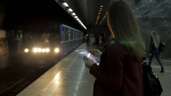 Dziewczyna w czerwonym płaszczu, stacji metra i czeka na pociąg za pomocą smartfona lub tabletu. Kobieta za pomocą cellphone i stojącą w mieście metra staton. — Zdjęcie stockowe