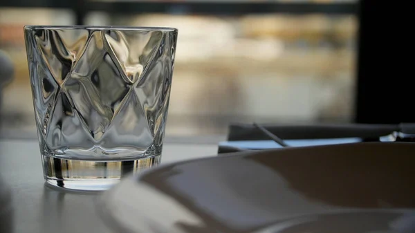 Faceted glass of water on nature background. Clear faceted glass with whiskey on a dark wooden table, close-up. Empty faceted glass — Stock Photo, Image