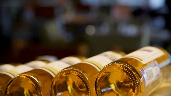 Botellas borrosas de vino blanco y rosa están muy bien dispuestos en una fila en un estante en un gran supermercado. Fondo abstracto brillante ideal para cualquier diseño. Estante en bodega con botellas de descanso — Foto de Stock