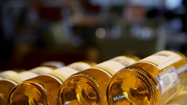 Botellas borrosas de vino blanco y rosa están muy bien dispuestos en una fila en un estante en un gran supermercado. Fondo abstracto brillante ideal para cualquier diseño. Estante en bodega con botellas de descanso — Foto de Stock