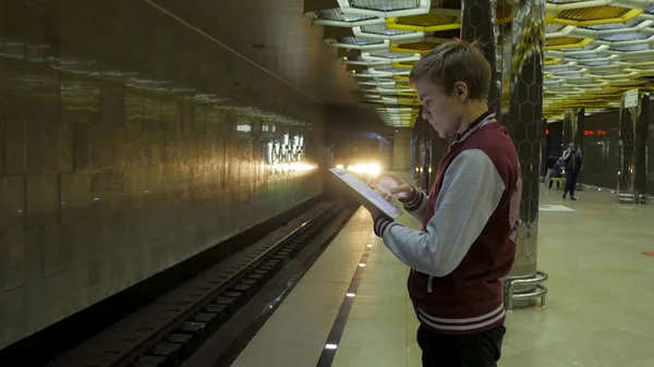 Man using touchpad or smartphone when he waits for train at subway station. Lonely young man with smartphone shot from profile at subway station with blurry moving train in background. — Stock Photo, Image