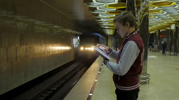 Man using touchpad or smartphone when he waits for train at subway station. Lonely young man with smartphone shot from profile at subway station with blurry moving train in background. — Stock Photo, Image