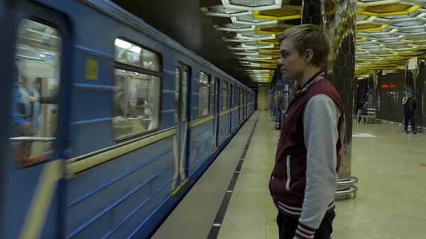 彼は地下鉄の駅で電車を待つときにタッチパッドやスマート フォンを使用している人。スマート フォンで孤独な若い男がプロファイルからぼやけて背景で動いている電車と地下鉄の駅で撮影. — ストック写真
