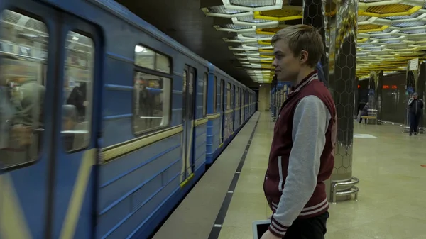 Man using touchpad or smartphone when he waits for train at subway station. Lonely young man with smartphone shot from profile at subway station with blurry moving train in background. — Stock Photo, Image