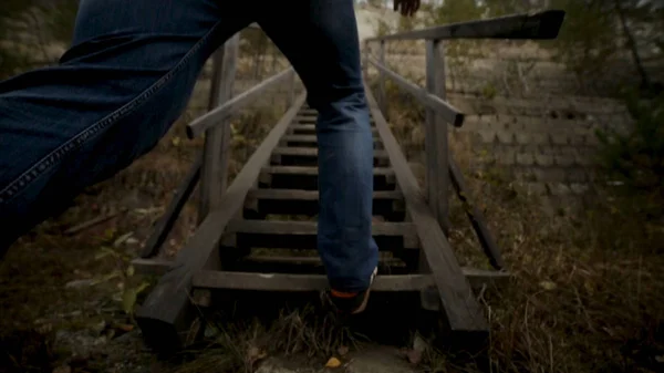 Hombre hombre subiendo escaleras. Filmación. Los antiguos escalones de madera en una colina que se eleva a cada lado de la hierba. Escaleras de madera en una colina de hierba —  Fotos de Stock