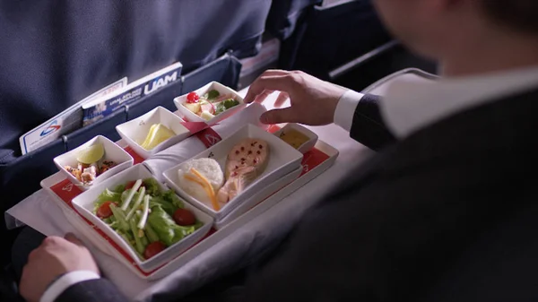 Midsection of stewardess holding tray with airplane food on blue background. Stewardess brought lunch, businessman, first class, high level of service on the plane — Stock Photo, Image