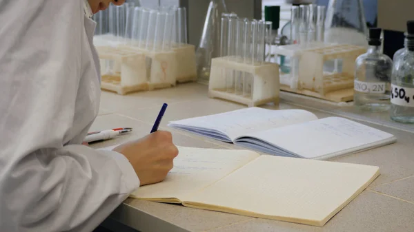 Médico jovem cientista a tomar notas. Cientista feminina toma notas em segundo plano são os tubos — Fotografia de Stock