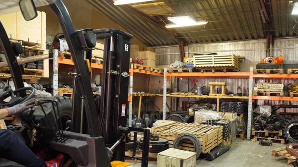 Forklift driver in protective vest driving forklift at warehouse of freight forwarding company. Man on the forklift drives into the garage